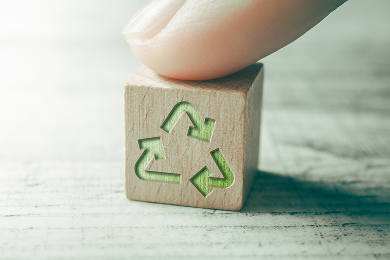 Green Recycling Icon On A Wooden Block On A Table, Touched By Finger